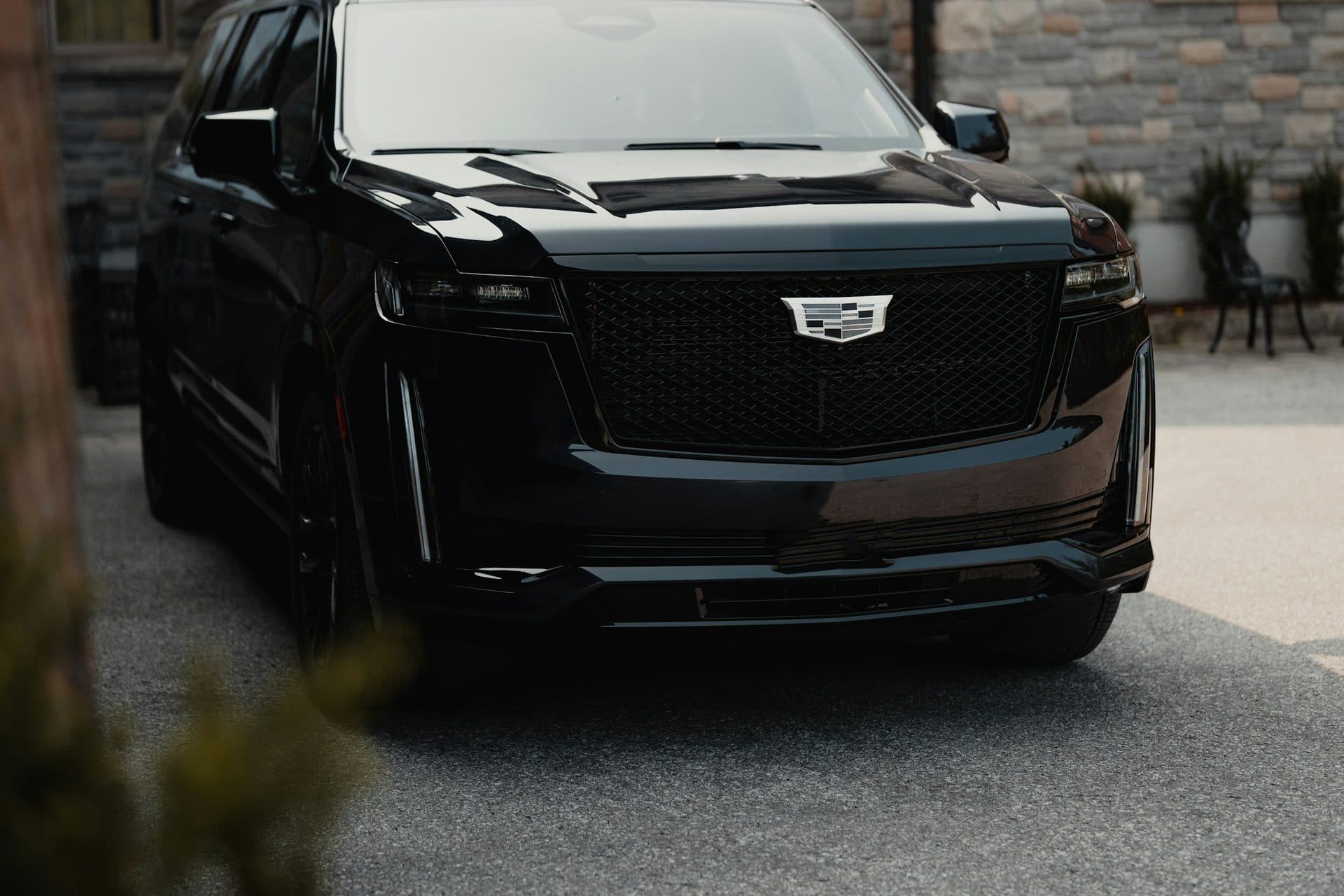 Front of a black Cadillac Escalade parked on a stone-paved drive