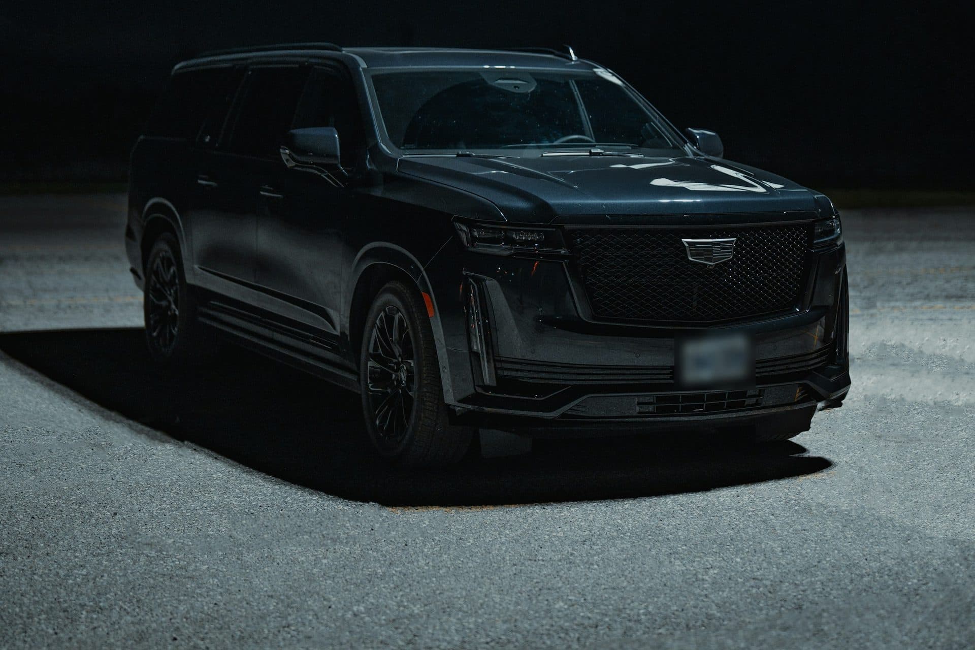 Black Cadillac Escalade parked in a pool of light at night