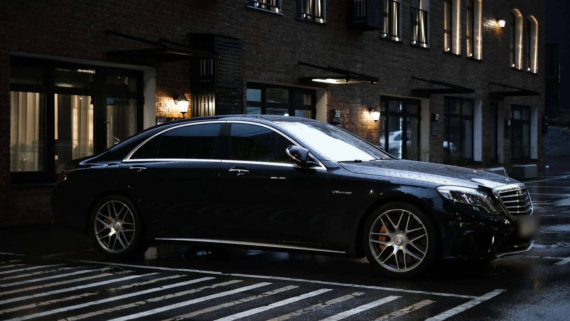 Black Mercedes-Benz S-Class sedan parked on a wet street at night